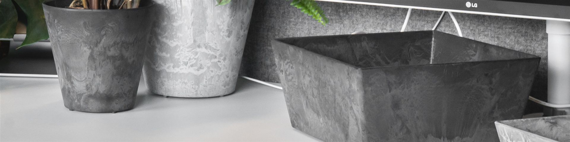 Eine graue Artstone-Ella-Schale steht als Ablage auf einem Schreibtisch, daneben bepflanzte Artstone-T&ouml;pfe
