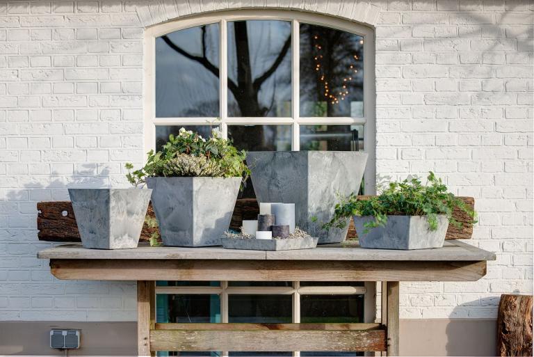 Graue eckige Artstone Ella T&ouml;pfe und K&auml;sten bepflanzt auf einem Gartentisch vor einem Fenster