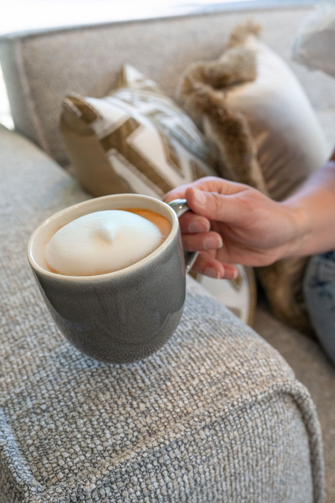 Eine Hand h&auml;lt einen gro&szlig;en Becher Savannah Shadow mit Milchschaum